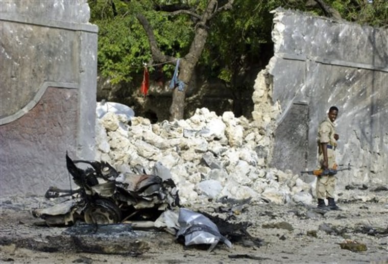A Somali government soldier stands near the remains of the vehicle which exploded in Mogadishu on Tuesday.